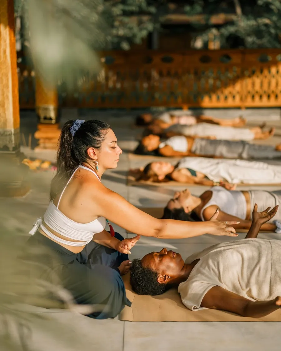 Praticienne guidant une relaxation collective, passant entre les participants allongés